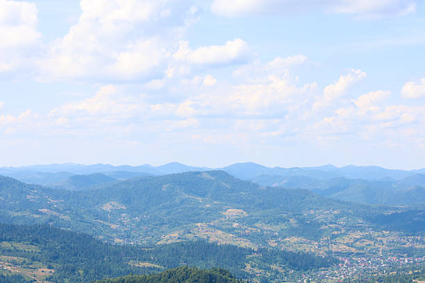 A massive mountain range, covered with dense forests, stretches to the horizon, where it dissipates into a light haze. The image illustrates the majesty, tranquility, and natural beauty of the mountains,
