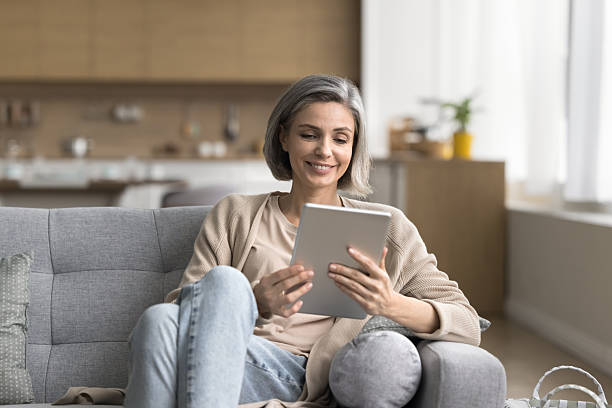 istock Smiling mature female using digital tablet on couch at home 2227975333