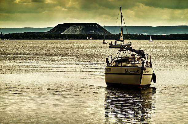 Mardorf, germany, june 29, 2025, sailboats gliding across the tranquil waters of steinhuder meer in lower saxony, with the striking kalihalde salt mountain rising under a dramatic sky