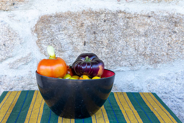 A bowl of tomatoes and onions sits on a table. The bowl is black and the table is green and yellow