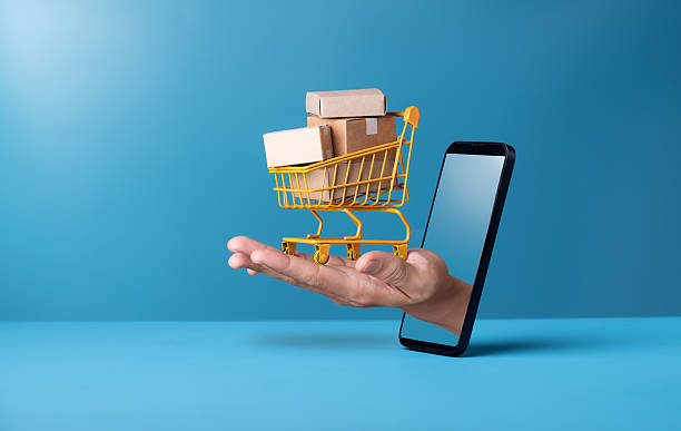 Mini shopping cart with cardboard boxes on hand through smartphone on blue background. Delivery service,online shopping concept. stock photo