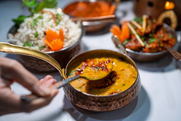 Close-up of hand scooping Indian dahl curry from a copper bowl during a traditional meal.