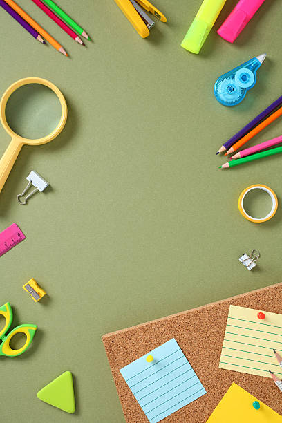 istock Colorful stationery assortment on green background with corkboard and sticky notes. Includes pencils, highlighters, scissors, magnifier, triangle eraser, stapler, tape, and binder clips. 2227991935