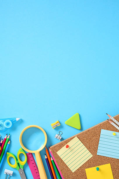 istock Top view school supplies on blue background with corkboard. Includes colored pencils, scissors, magnifier, ruler, sticky notes, correction tapes, clips, and triangle eraser. 2227992105