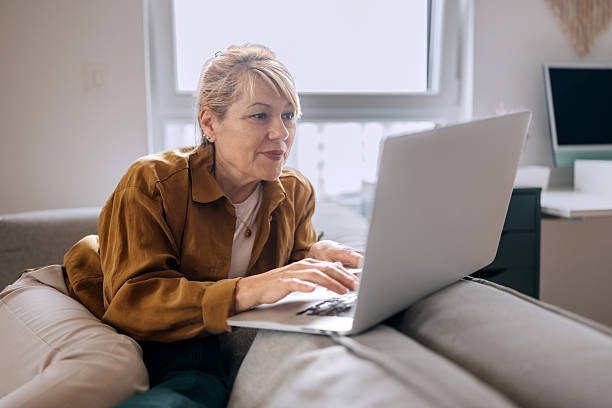 istock Senior woman using laptop while relaxing on a sofa at home 2227994829
