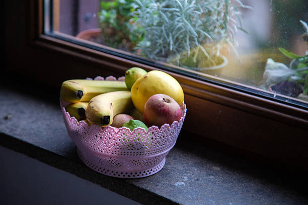 A bowl full of assorted fruit is sitting on a window sill today