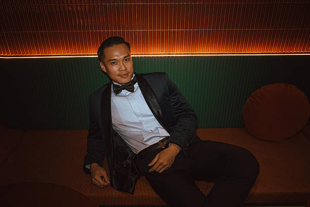 istock Confident Asian Man in Tuxedo Relaxing on Lounge Sofa 2228002840