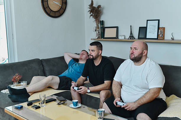 istock Male Relaxing on Sofa While Watching Two Gamer Friends Compete In Video Game 2228004928