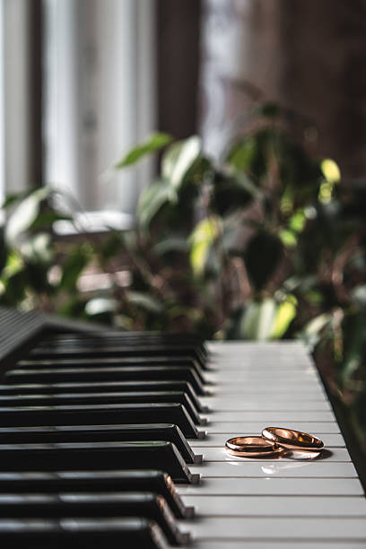 wedding rings gleam on surface black and white piano keys, surrounded by soft natural light and rich greenery, creating an intimate and romantic atmosphere. vertical. close up.