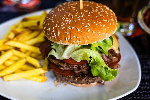 Close-up of a freshly made double cheeseburger with lettuce tomato and melted cheese served on a sesame seed bun next to a portion of crispy golden fries. Delicious fast food meal captured in natural light.