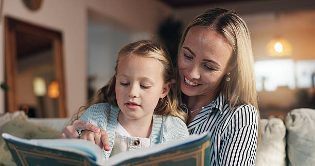 istock Mom, girl and reading book on sofa, learning and support with development, love and bonding in lounge. People, mother and daughter with literature, education and helping hand on couch at family house 2228023742