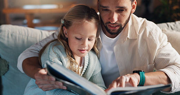 istock Dad, girl and reading book on sofa, learning and support with development, love and bonding in lounge. People, father and child with literature, education and helping hand on couch at family house 2228023768