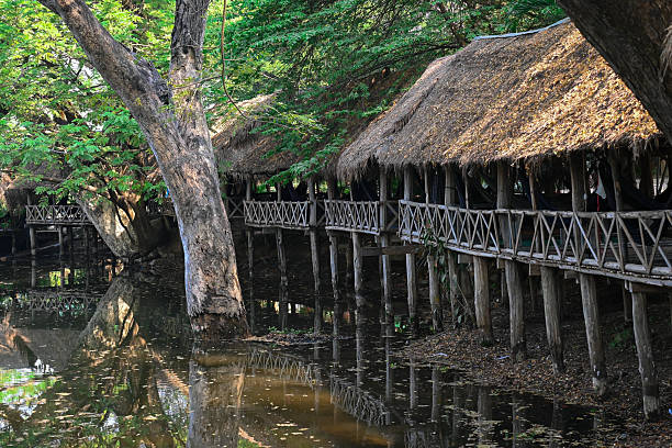 istock Traditional wooden huts with thatched roofs built on stilts over water 2228027916