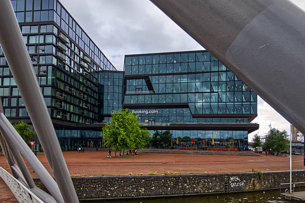 Amsterdam, netherlands, july 7,2025, modern office building with glass facade reflecting cloudy sky, seen from a bridge over canal in amsterdam, netherlands, with metal beams framing the scene