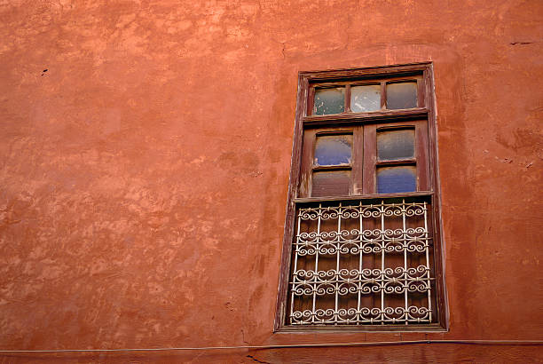 istock Old wooden window with metal bars on a red stucco wall 2228032217