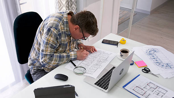 istock A nerd with glasses hunched over his architectural masterpiece. A man is sitting at a table with a laptop and building drawings 2228037184