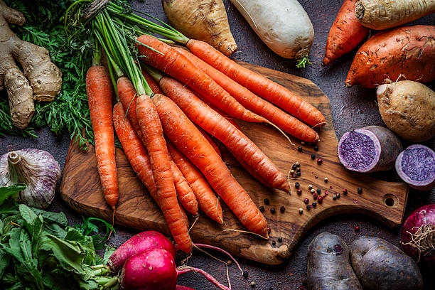 Fresh organic carrots and other root vegetables shot from above on kitchen table. Healthy eating or vegetarian food.