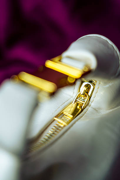 The image showcases a detailed close-up of a white leather handbag's gold zipper. The focus is on the zipper's intricate details and the contrast between the white leather and the gold hardware.