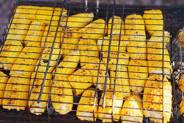 A close-up shot of grilled sweet corn on a metal tray, preparing for sale at an Asian night market.