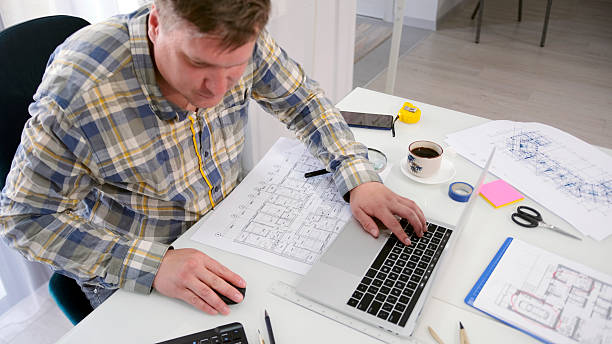 istock The architect is working on a new construction project for a business center. A man is sitting at a table with a laptop, building drawings 2228052390