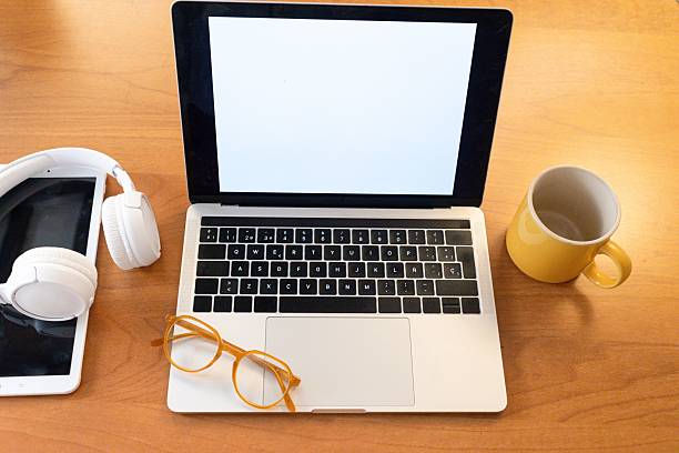 Workspace with a laptop, headphones, glasses, and a yellow mug on a wooden desk.