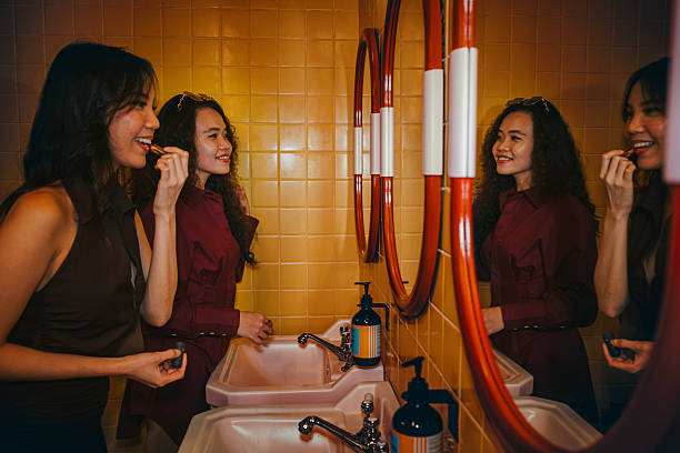 Two Young Asian Women Applying Makeup Together at a Restroom Mirror