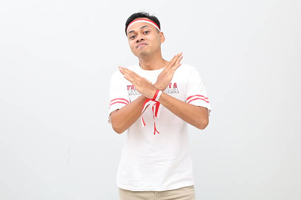 Indonesian man with red and white ribbon, celebrating Indonesian independence day while standing with crossed arms, refusing or prohibiting something, smiling looking at the camera.
