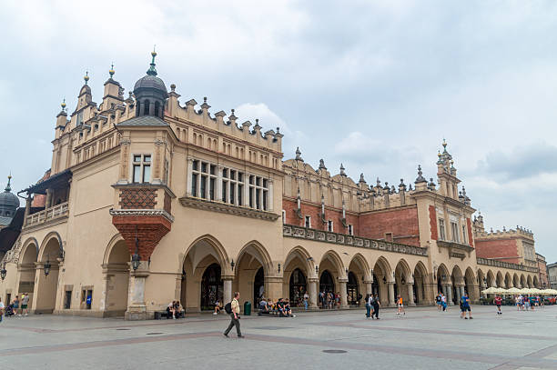 Many tourists visible near the Kraków Cloth Hall (Sukiennice), located in the heart of Rynek Główny Square, a Renaissance trading hall that has been a centerpiece of Kraków's commerce since the 14th century. Originally a center for trading textiles, it was rebuilt in the 16th century after a fire, featuring elegant arcades and an attic with decorative masks. Today, the ground floor houses stalls selling traditional Polish crafts and souvenirs.