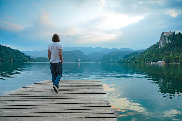 Woman admiring lake Bled at dusk from wooden pier on a lakeshore.