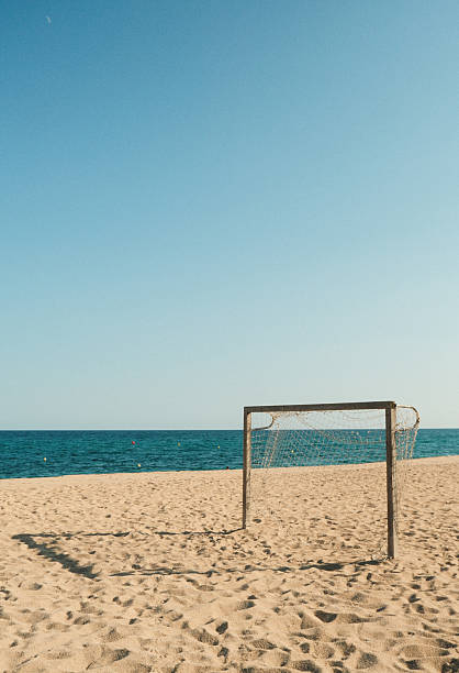 Empty soccer goal stands on a sandy beach, inviting players to a seaside match under the clear blue sky