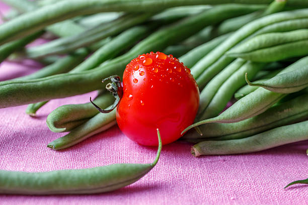 Focus on the sparkling tomato with water droplets. The vegetables lie on a pink linnen cloth