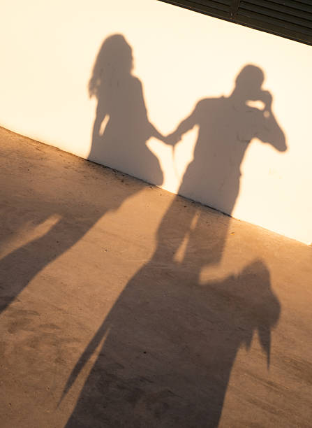 Shadow of a young couple holding hands while capturing a selfie, projected on a wall during sunset, beautifully illustrating a romantic moment filled with love and connection