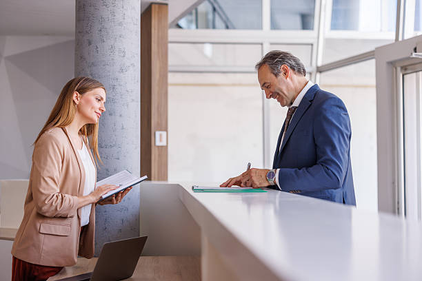 istock Businessman signing documents at reception desk with assistant 2228092981