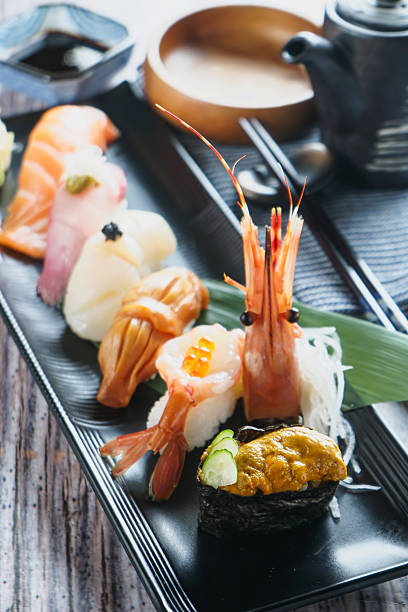 Assorted Sushi Platter including nigiri with salmon, scallops, sea urchin, and shrimp, along with rolls and sashimi in black tray side view of japanese cousin