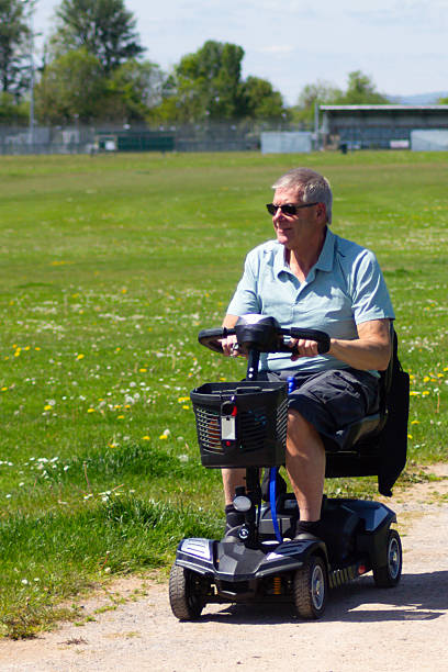 Mobility scooter freedom, middle aged man enjoys driving his disability scooter along a pathway in the countryside of Shropshire. The electric scooter allows him independence to move despite his physical problems and disabilities.