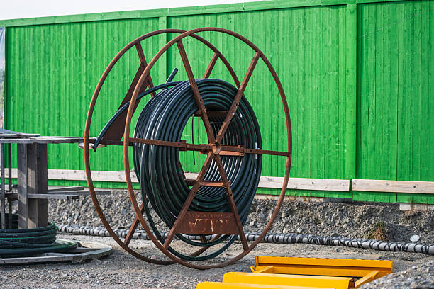 Large industrial cable spool near green fence.