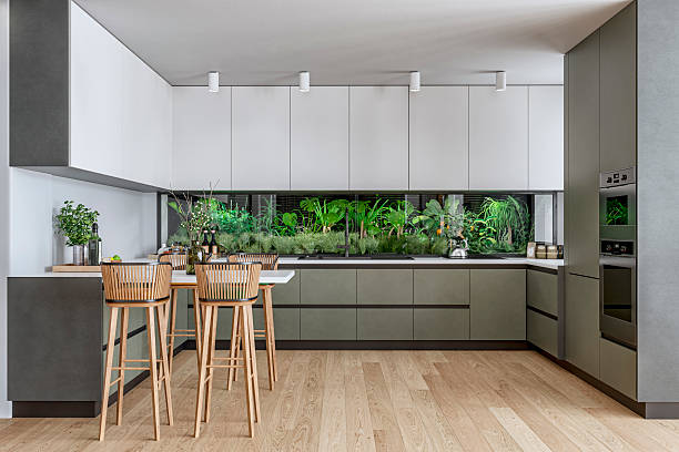 istock A modern kitchen with  muted green and white cabinetry, lush indoor green wall as backsplash, a bar-height dining area with wooden stools on hardwood floor 2228109632