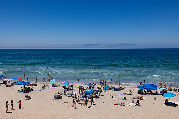 Encinitas, California, USA – June 27, 2025: People enjoying a sunny summer day at Moonlight Beach with blue water, gentle surf, and tourists relaxing, swimming, and playing on the sand. This image is for editorial use only.