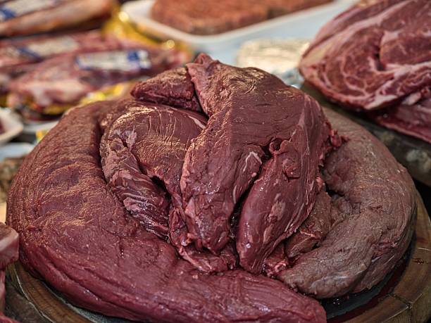 A close-up view of raw beef steak served on a ceramic plate in a restaurant. A chef's hand with a knife slices the fresh meat before cooking. Realistic food photography showing traditional meal preparation with natural light and authentic setting.