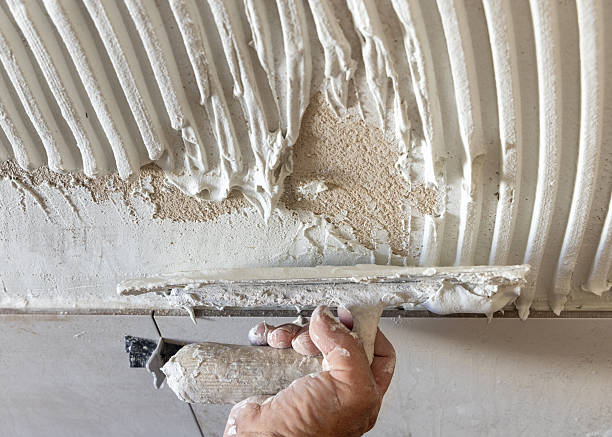 istock Craftsman spreads wall tile adhesive with trowel a house wall, hand closeup. Construction process 2228121082