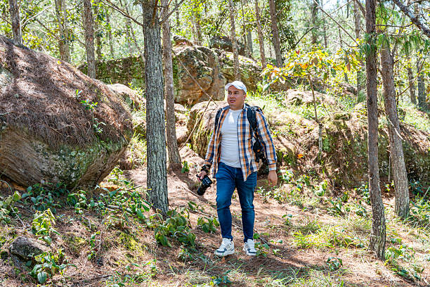 Latin American male photographer walking calmly through a dense forest, observing the environment. Scene reflects nature exploration, creativity, and outdoor inspiration, perfect for travel and lifestyle visuals