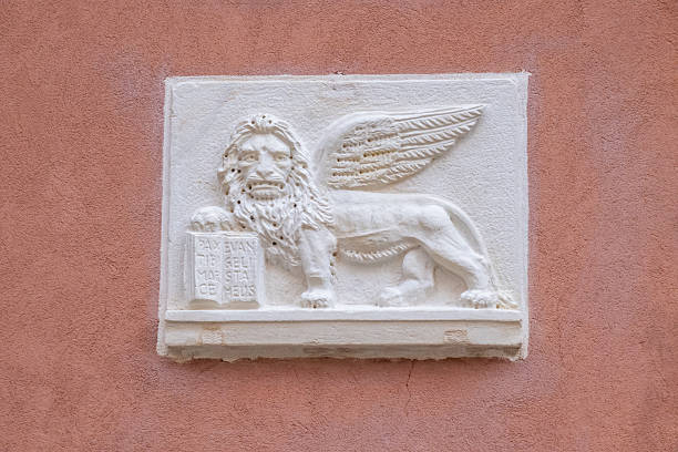Venice, Italy - 12 October 2024: A white stone relief of the Winged Lion of Saint Mark, symbol of Venice, carved on a pastel-colored wall.