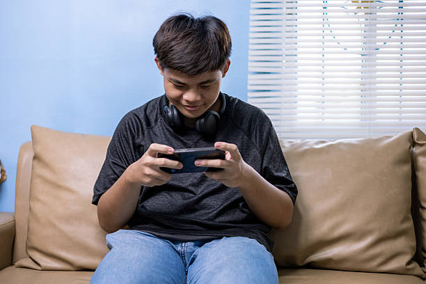 istock Asian guy teenager sitting on sofa at home relax using mobile phone app typing text browsing message, gen z checking social media on webpage, happiness lifestyle digital communication concepts 2228124466