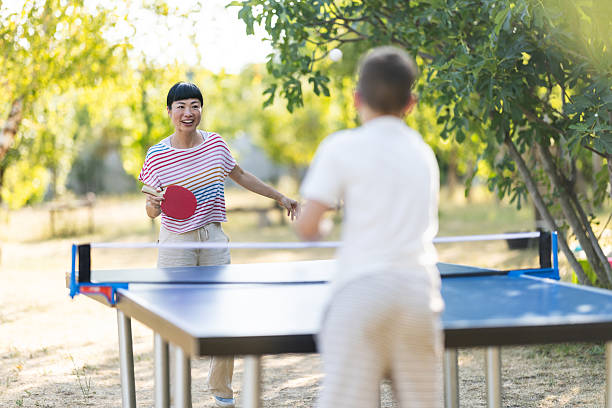Cheerful Japanese woman playing table tennis with a Caucasian boy in backyard
