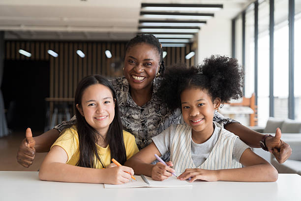 Female teacher teaching student in classroom, happy smiling during take note or lecture on book and looking to camera