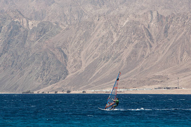 Dahab, Egypt - May 18, 2019: Windsurfer cuts through Red Sea waters with rugged Sinai cliffs rising behind. High quality photo