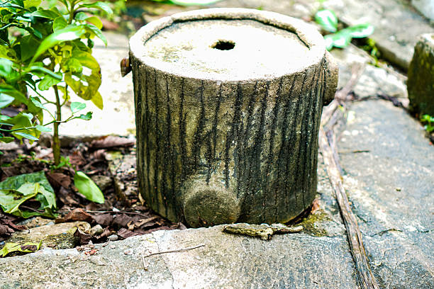 A creatively designed outdoor garden stool made from cement, shaped and textured to resemble a tree stump. Surrounded by natural elements like green plants and stone tiles, the scene conveys a rustic and eco-friendly aesthetic, perfect for nature-inspired outdoor seating or decoration.