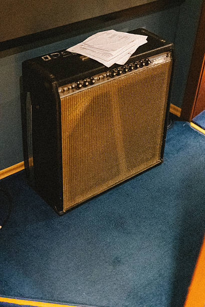 A guitar amplifier placed in the corner of a recording studio, with sheet music resting on top. The amp shows signs of use, contributing to the authentic and lived-in feel of the creative space. Ideal for themes related to music production, rehearsal rooms, or audio equipment.