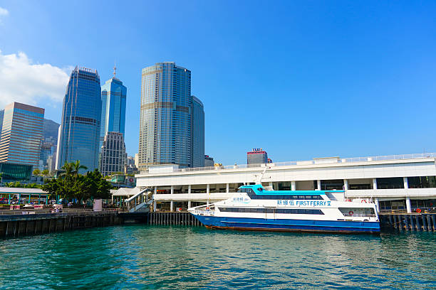 First ferry is moored busy waterfront terminal, alongside modern skyscrapers and under a vibrant blue sky. China, Hong Kong 20 january 2025.