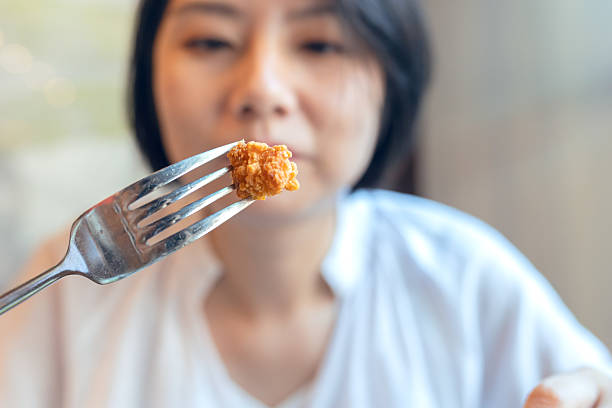 An Asian woman eating fried chicken nuggets with a fork